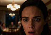 My phone buzzed, stuck under my mom’s dining table. As I bent down, a wax-sealed envelope slid toward me. A woman I’d never seen whispered, “Please read it.” My heart raced. I opened it with shaking hands. When the words came into view… I understood why the entire room suddenly went silent.