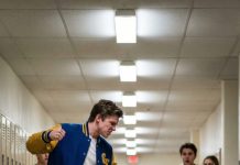 He laughed as he kicked her crutches away, sending her crashing onto the crowded hallway floor while phones lifted to record. “What’s she going to do about it?” he mocked. She didn’t cry—she just looked toward the entrance. Seconds later, the double doors slammed open, and the color drained from his face when he saw who was striding down the corridor.